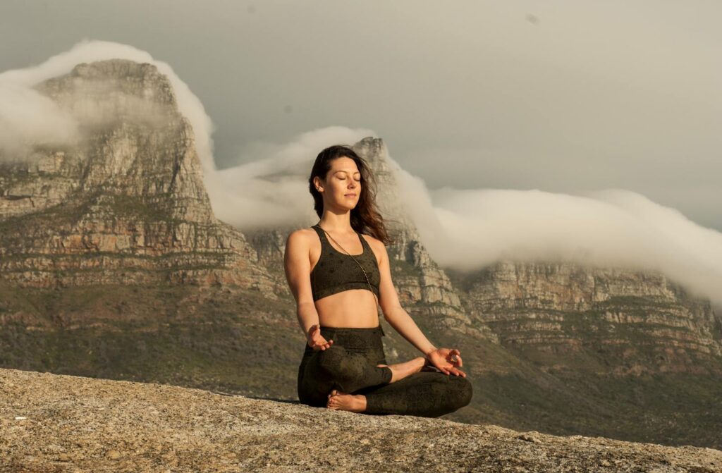 Woman in Black Sports Bra and Black Pants Sitting on Rock